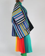Cargar imagen en el visor de la galería, A model is shown from the side wearing a vibrant, multicolored striped quilted jacket with wide lapels, paired with a matching rainbow pleated skirt.