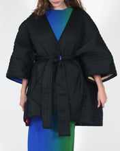 Cargar imagen en el visor de la galería, A model wearing a black quilted kimono-style wrap jacket with wide sleeves and a self-tie belt, layered over a blue and green gradient top and skirt, against a plain white background.
