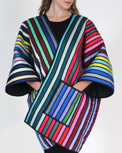 Cargar imagen en el visor de la galería, A model wearing a colorful striped quilted coat over a black dress, shown from the neck down against a light gray studio background
