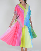 Charger l'image dans la galerie, A woman modeling a vibrant, multi-colored pleated wrap dress with short flutter sleeves and a pleated skirt, featuring rainbow stripes of pink, yellow, green, blue, and purple against a plain light gray background.

